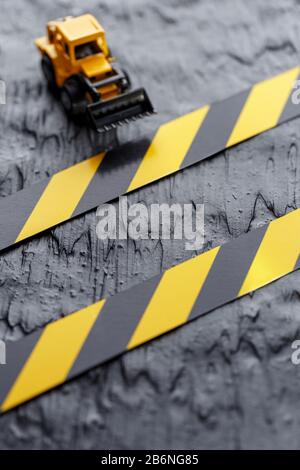 Gelbe Planierraupe auf schwarzem Hintergrund. Schwarzes und gelbes Zaunband vor dem Hintergrund des KONZEPTS. Geschäft, Reparatur, Dienstleistungen. Stockfoto