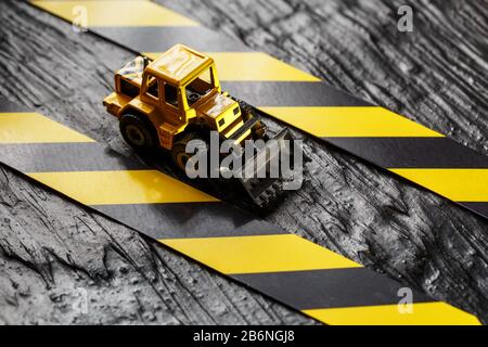 Spielzeugbagger gelb auf schwarzem Hintergrund. Bandlineal schwarz und gelb auf dem Hintergrund. KONZEPT. Geschäft, Reparatur, Dienstleistungen. Stockfoto