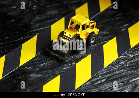 Spielzeugbagger gelb auf schwarzem Hintergrund. Bandlineal schwarz und gelb auf dem Hintergrund. KONZEPT. Geschäft, Reparatur, Dienstleistungen. Stockfoto