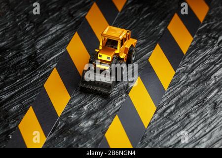 Gelbe Planierraupe auf schwarzem Hintergrund. Schwarzes und gelbes Zaunband vor dem Hintergrund des KONZEPTS. Geschäft, Reparatur, Dienstleistungen. Stockfoto