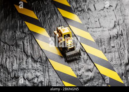Spielzeugbagger gelb auf schwarzem Hintergrund. Bandlineal schwarz und gelb auf dem Hintergrund. KONZEPT. Geschäft, Reparatur, Dienstleistungen. Stockfoto