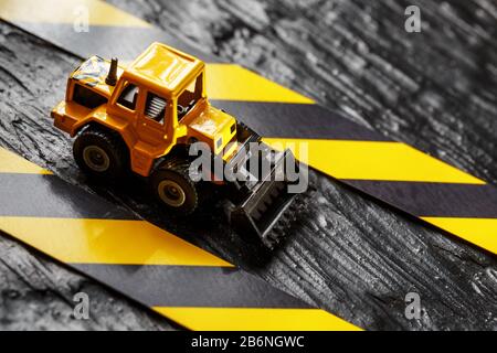 Spielzeugbagger gelb auf schwarzem Hintergrund. Bandlineal schwarz und gelb auf dem Hintergrund. KONZEPT. Geschäft, Reparatur, Dienstleistungen. Stockfoto
