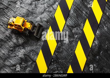 Spielzeugbagger gelb auf schwarzem Hintergrund. Bandlineal schwarz und gelb auf dem Hintergrund. KONZEPT. Geschäft, Reparatur, Dienstleistungen. Stockfoto