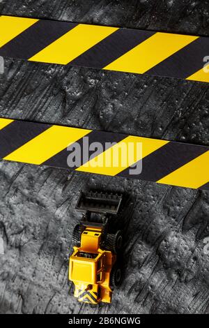 Spielzeugbagger gelb auf schwarzem texturalem Hintergrund. Band Fechten schwarz gelb vor dem Hintergrund des KONZEPTS. Vertikaler Rahmen Stockfoto