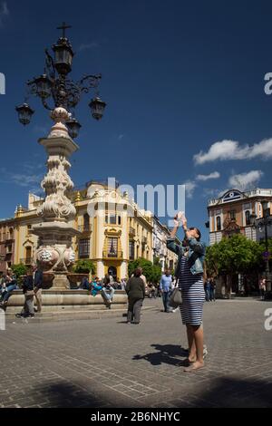 Touristen, die Fotos mit einem Handy neben der Brunnenampel am Virgen de los Reyes Platz, Sevilla, Spanien machen Stockfoto