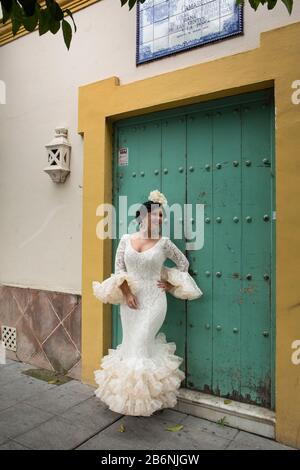 Dame, die ein sevillian Kostüm trägt, posiert an einem Gebäudeeingang der Betis St im Viertel Triana, Sevilla, Spanien Stockfoto