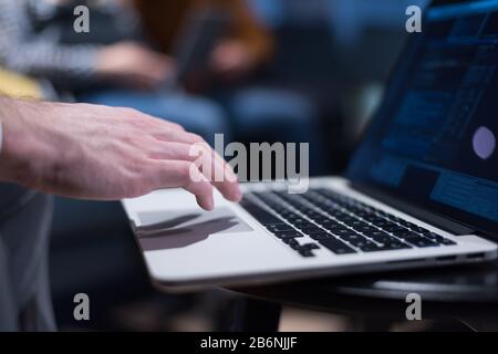Zugeschnittenes Bild eines jungen Mannes, der an seinem Laptop im Büro arbeitet, Rückansicht des Geschäftsmannes, der mit dem Laptop am Büroschreibtisch beschäftigt ist, junger männlicher Stehbolzen Stockfoto