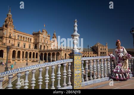 Die Dame, die ein sevillianische Kostüm trägt, posiert über eine mit Fliesen bedeckte Brücke am España-Platz im María Luisa Park, Sevilla, Spanien Stockfoto