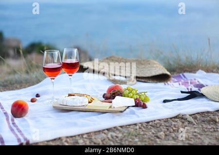 Am Sommerabend können Sie ein romantisches Picknick mit einer Brille Wein mit Obst und Käse auf der Decke an der felsigen Küste machen Stockfoto