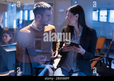 Zwei fokussierte junge Geschäftskollegen, die über ein digitales Tablet sprechen, während sie ein Treffen in einem modernen Büro haben Stockfoto