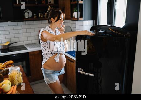 Hungrige schwangere Frau für Lebensmittel im Kühlschrank auf der Suche Stockfoto