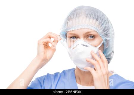 Porträt einer blauäugigen Frau in einer chirurgischen Kappe, die die Atemmaske vor weißem Hintergrund auf das Gesicht legt Stockfoto