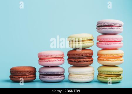 Makkaroni-Kekse verschiedener Farben sind in Form von Pyramidenstufen auf blauem Grund angeordnet. Freier Speicherplatz. Das Konzept des Minimalismus Stockfoto