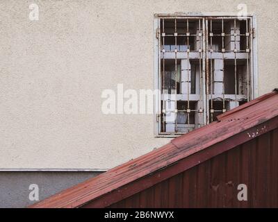 Eine gelbe Wand, auf der ein altes schmutziges Fenster mit einem Metallgrill schräg mit geriffeltem rostigen Eisen verschlossen ist. Platz für eine Beschriftung. Stockfoto