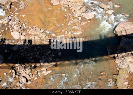 Mit Blick auf den Schatten einer Fußgängerbrücke, die den Reedy River überquert, liegt Greenville, South Carolina Stockfoto