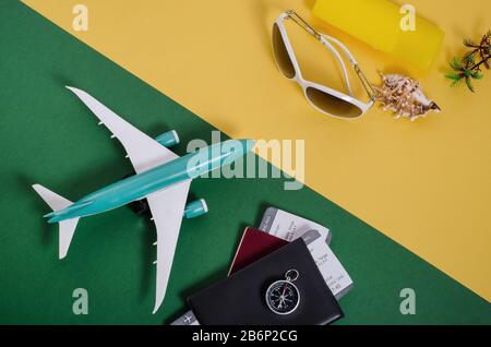 Planung, Vorbereitung auf Reisen, Urlaubsreisenkonzept. Flugzeug mit Pässen und Tickets auf grünem Hintergrund vor Strandartikeln auf gelbem B. Stockfoto