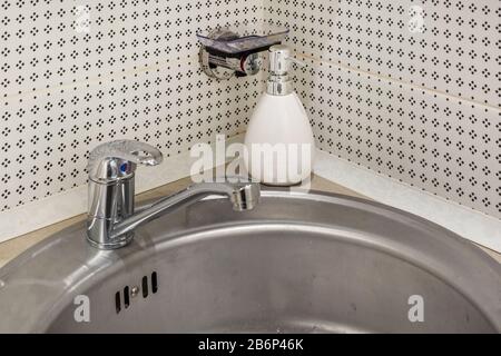 Seife und Shampoo-Dispenser in der Nähe Von Keramischen Wasserhahn-Spüle mit Hahn im teuren Loft-Bad oder in der Küche Stockfoto