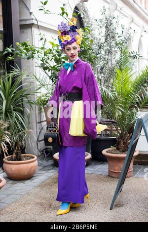 London, Großbritannien - febryary 15 2020: Modische Menschen auf der Straße . Straßenstil. Ein Mann in einem violetten Kimono mit einem hellen Make-up und einer Krone aus Eimell Stockfoto