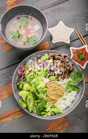 Gesunde Lebensmittel aus biologischem asien. Buddha-Schüssel mit Lachs-Fischsuppe, Salat, Reis mit Pesto, Spinatblättern, grünen Bohnen, Rindfleisch mit Teriyaki-Sauce. Vertikal Stockfoto