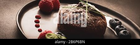 Schokoladenmuffins mit Himbeeren und Blaubeeren auf schwarzem Teller mit Hintergrundbeleuchtung, Lebensmittelfoto mit Retro-End-Weichfarben Stockfoto