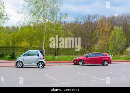 Foto des Parkplatzes mit kleinen weißen und roten Autos in der Nähe des Parks Stockfoto