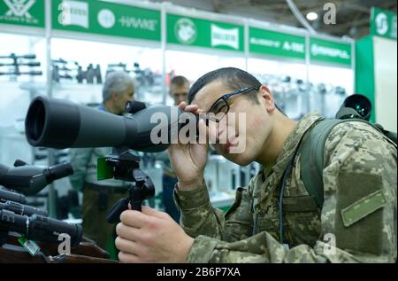 Junger Mann in Militäruniform, der durch tragbares monokulares Teleskop, Waffengeschäft blickt. Oktober 2019. Kiew, Ukraine Stockfoto