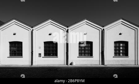 Altmodischer Fabrikschuppen mit blassrosa Fassade am blauen Himmel, Zick-Zack-Dach, Hydrant und Fenster in den südlichen Vororten von Mailand, Italien Stockfoto