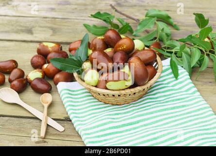 Geflochtener Becher mit reifen Früchten der Jujube (jujube real, chinesisches Datum, Capiinit, Jojoba, lat. Ziziphus jujujuba) auf einem alten Holztisch. Zwei Holzspoo Stockfoto