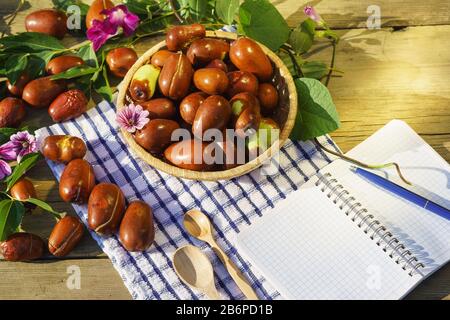 Korbkorb mit Ziziphus echten Früchten, Kopfsteinpflaster, Unabi, Capiente, Marmalade, Capiinit, Jojoba, chinesisches Datum und Notepad zum Schreiben in Sonnenlicht. Stockfoto