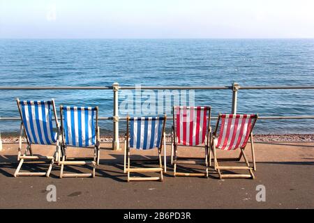 Sidmouth, South Devon/Großbritannien: Reihe von blau-weiß/rot-weiß gestreiften Liegestühlen am Meer an der Esplanade Stockfoto