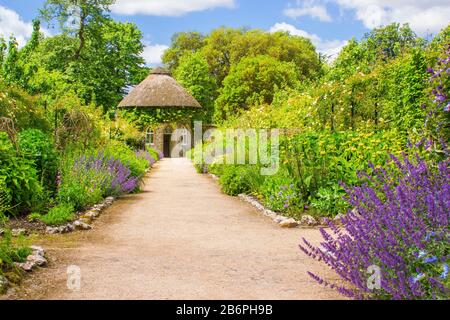 Das 19. Jahrhundert strohgedeckten runden Haus, umgeben von schönen Blumenbeeten und Schotterwege, das in der ummauerten Garten in West Dean Gärten in West Sussex Stockfoto