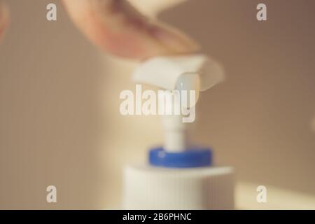 Fingerberührung mit einer Flüssigseifenspender. Weißes Gel fällt aus der Flasche. Stockfoto