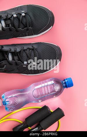 Schwarze Sportschuhe, Springseil und Flasche Wasser auf pinkfarbenem Hintergrund. Draufsicht. Stockfoto