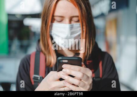 Frau in Gesichtsschutzmaske mit dem Telefon an einem öffentlichen Ort. Coronavirus, COVID-19 Spread Prevention Concept, verantwortungsbewusstes Sozialverhalten eines ci Stockfoto