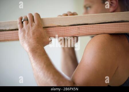 Männlicher Bauherr, der zwei Holzbohlen trägt. Stockfoto