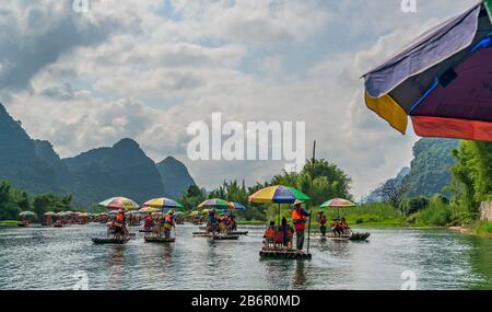 Yangshuo, China - August 2019: Touristen, die auf Bambusflößen sitzen, gelenkt von Führern mit langen Stöcken am malerischen und schönen Fluss Yulong Stockfoto