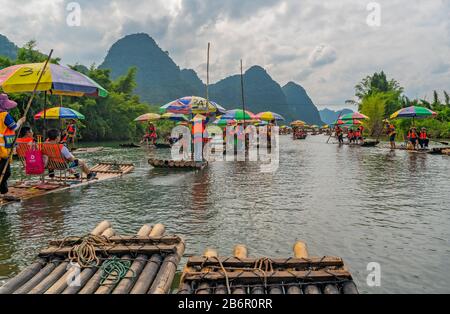 Yangshuo, China - August 2019: Touristen, die auf Bambusflößen sitzen, gelenkt von Führern mit langen Stöcken am malerischen und schönen Fluss Yulong Stockfoto