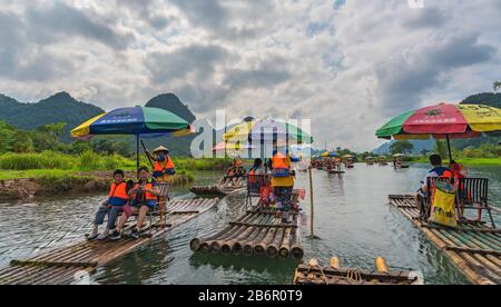 Yangshuo, China - August 2019: Touristen, die auf Bambusflößen sitzen, gelenkt von Führern mit langen Stöcken am malerischen und schönen Fluss Yulong Stockfoto