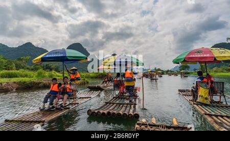 Yangshuo, China - August 2019: Touristen, die auf Bambusflößen sitzen, gelenkt von Führern mit langen Stöcken am malerischen und schönen Fluss Yulong Stockfoto