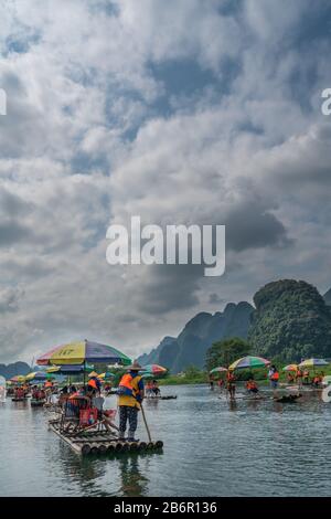 Yangshuo, China - August 2019: Touristen, die auf Bambusflößen sitzen, gelenkt von Führern mit langen Stöcken am malerischen und schönen Fluss Yulong Stockfoto