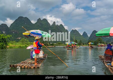 Yangshuo, China - August 2019: Touristen, die auf Bambusflößen sitzen, gelenkt von Führern mit langen Stöcken am malerischen und schönen Fluss Yulong Stockfoto