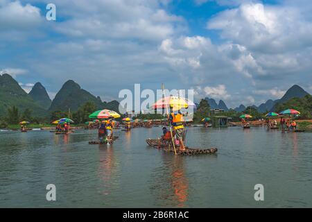 Yangshuo, China - August 2019: Touristen, die auf Bambusflößen sitzen, gelenkt von Führern mit langen Stöcken am malerischen und schönen Fluss Yulong Stockfoto