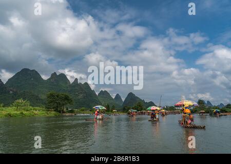 Yangshuo, China - August 2019: Touristen, die auf Bambusflößen sitzen, gelenkt von Führern mit langen Stöcken am malerischen und schönen Fluss Yulong Stockfoto