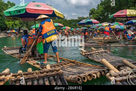 Yangshuo, China - August 2019: Touristen, die auf Bambusflößen sitzen, gelenkt von Führern mit langen Stöcken am malerischen und schönen Fluss Yulong Stockfoto