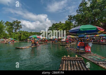 Yangshuo, China - August 2019: Touristen, die auf Bambusflößen sitzen, gelenkt von Führern mit langen Stöcken am malerischen und schönen Fluss Yulong Stockfoto