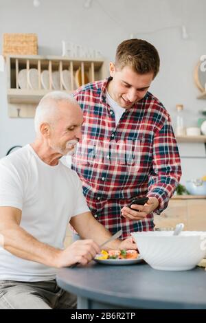 Junger Mann und leitender Vater telefonieren in der Küche Stockfoto