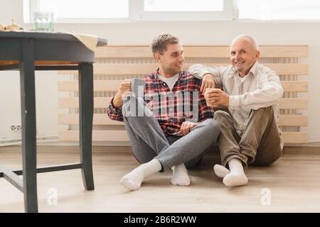 Ein Porträt von Erwachsenen hipster Sohn und Vater auf dem Boden drinnen, zu Hause zu sitzen. Stockfoto