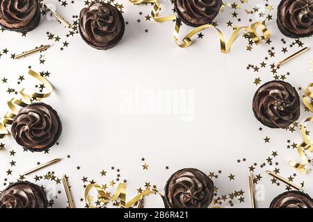 Schokoladenkuchen mit Schokoladenvereisung und gesprinklerten Goldglitzern auf weißem Hintergrund, dekoriert mit goldenem sternförmigen Konfetti, Kerzen und Party Stockfoto