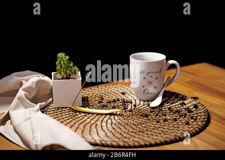 Weiße Keramikbecher mit den Worten "alles, was Sie brauchen, ist Liebe" voller schwarzer Kaffee auf einem Holztisch und Kaffeekörner Stockfoto