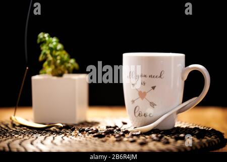 Weiße Keramikbecher mit den Worten "alles, was Sie brauchen, ist Liebe" voller schwarzer Kaffee auf einem Holztisch und Kaffeekörner Stockfoto